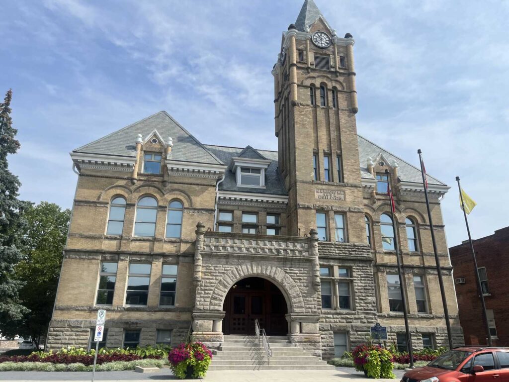 Front view of St. Thomas City Hall with its stone entrance arch, clock tower and summer flower planters