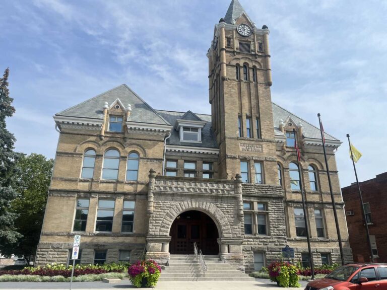Front view of St. Thomas City Hall with its stone entrance arch, clock tower and summer flower planters