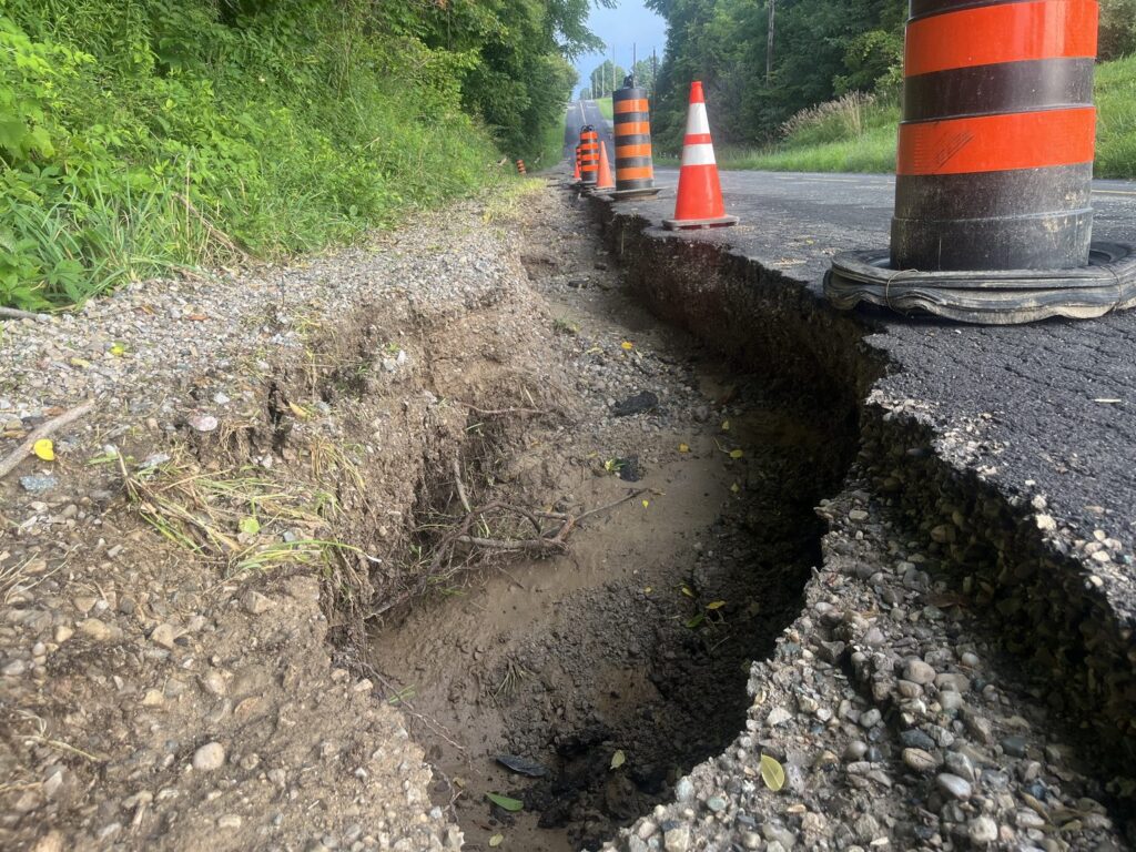 A washed-out section of the southbound lane of Mill Road in Southwold Township, marked off with traffic cones and barrels, with the road open beyond