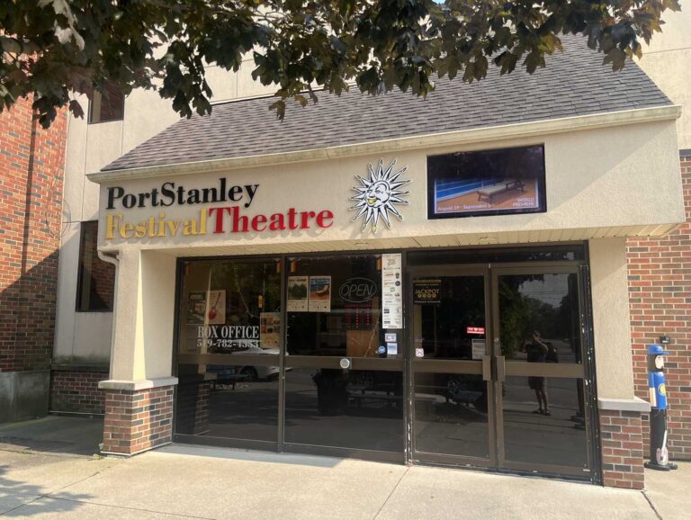 The entrance of the Port Stanley Festival Theatre, with its sun logo, box office signage and summer season posters in the glass doors.