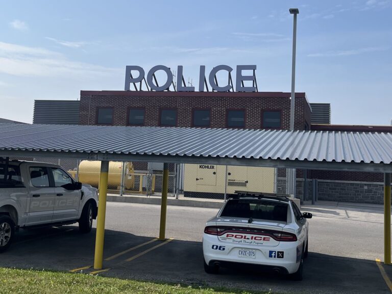 Rear of the St. Thomas Police Service headquarters with rooftop POLICE letters and a marked cruiser parked under a carport
