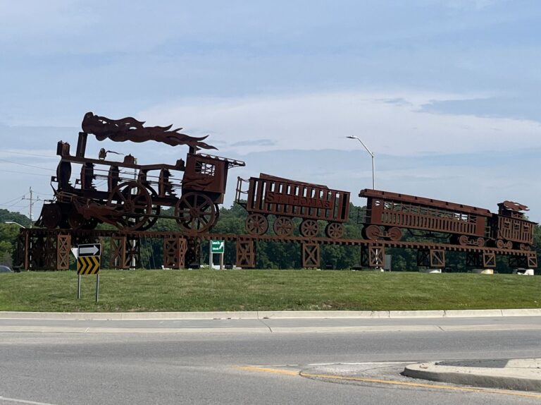 Rusted steel silhouette sculpture of a locomotive and rail cars lettered St. Thomas on a trestle base in the centre of a roundabout