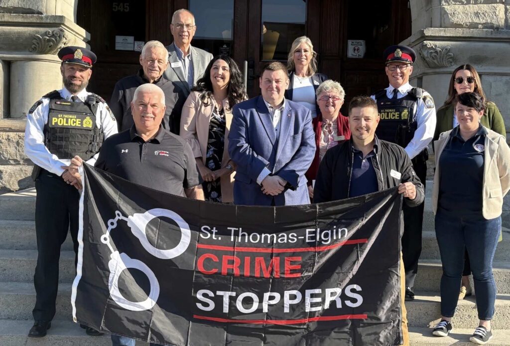Group holding a St. Thomas-Elgin Crime Stoppers banner on the front steps of St. Thomas City Hall, with St. Thomas Police officers and community members