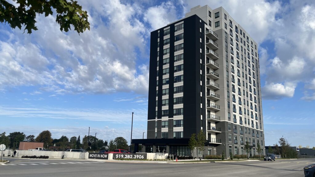 The 14-storey Highlands Tower apartment building at the corner of Talbot Street and First Avenue in St. Thomas, with a Move In Now banner on the low wall in front, October 2026