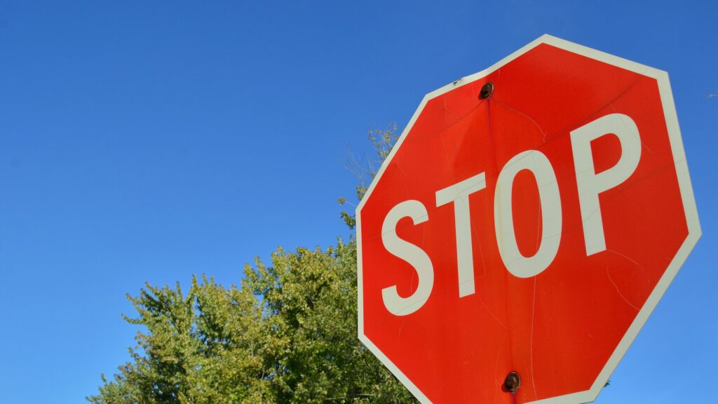 A red octagonal STOP sign seen from below against a clear blue sky, with green tree tops behind it